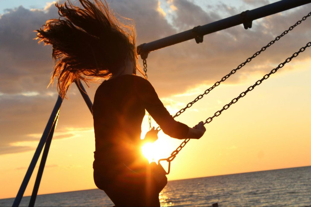 An individual enjoying a swing as the sun sets in the horizon.